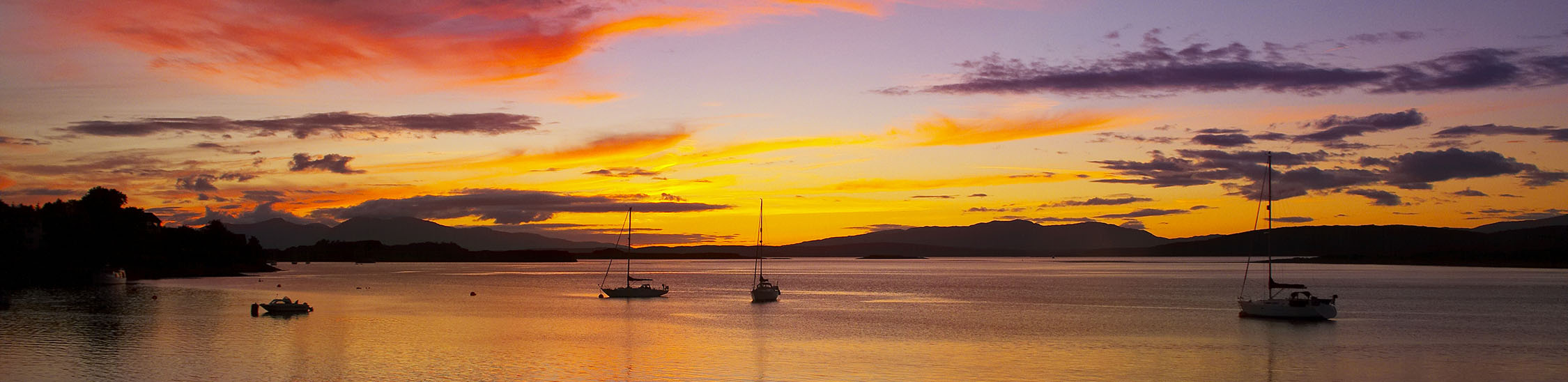 Picture-perfect scene: boats gently bobbing on the water, silhouetted against a fiery sunset.