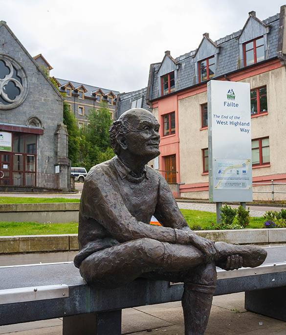 A statue of sore feet depicts a walker sitting on a bench while removing a boot after successfully completing the ninety six miles of the West Highland Way